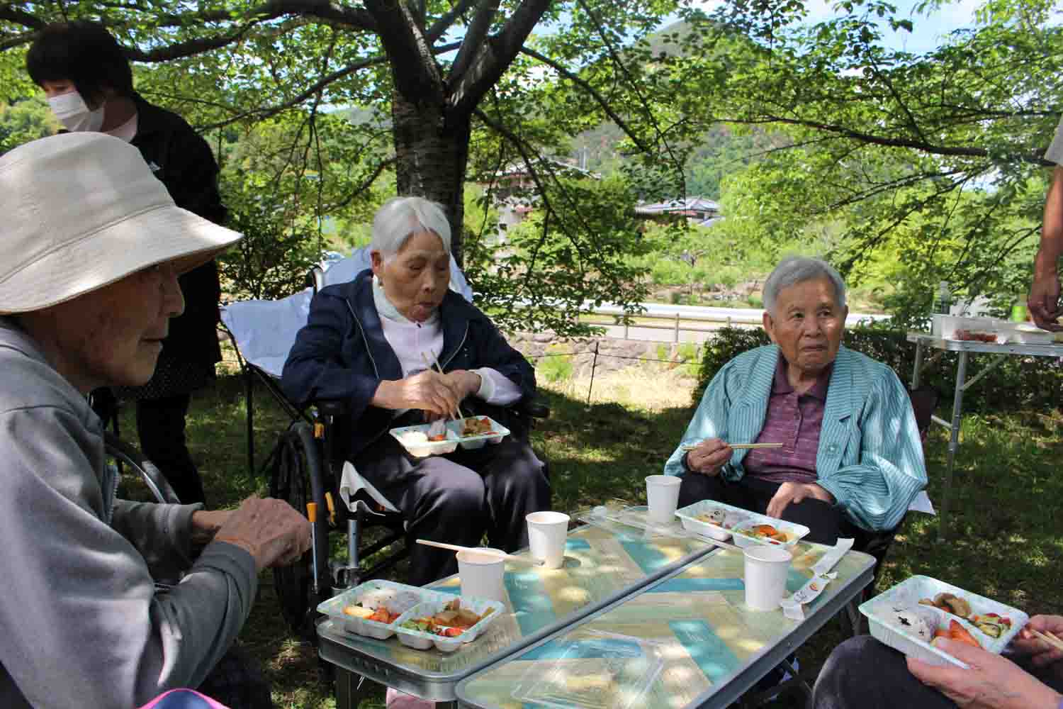 木陰で机を囲んでご飯を食べています。