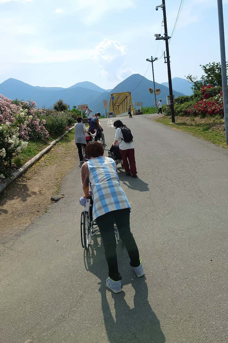 安全に坂道を下るため介護職員が後ろ歩きで車いすを引いています。