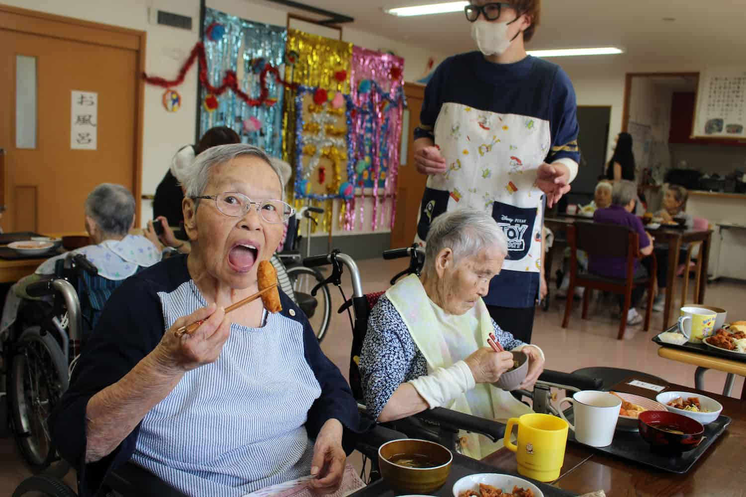 Mさんが大きい口を開けながらいなり寿司を食べています。