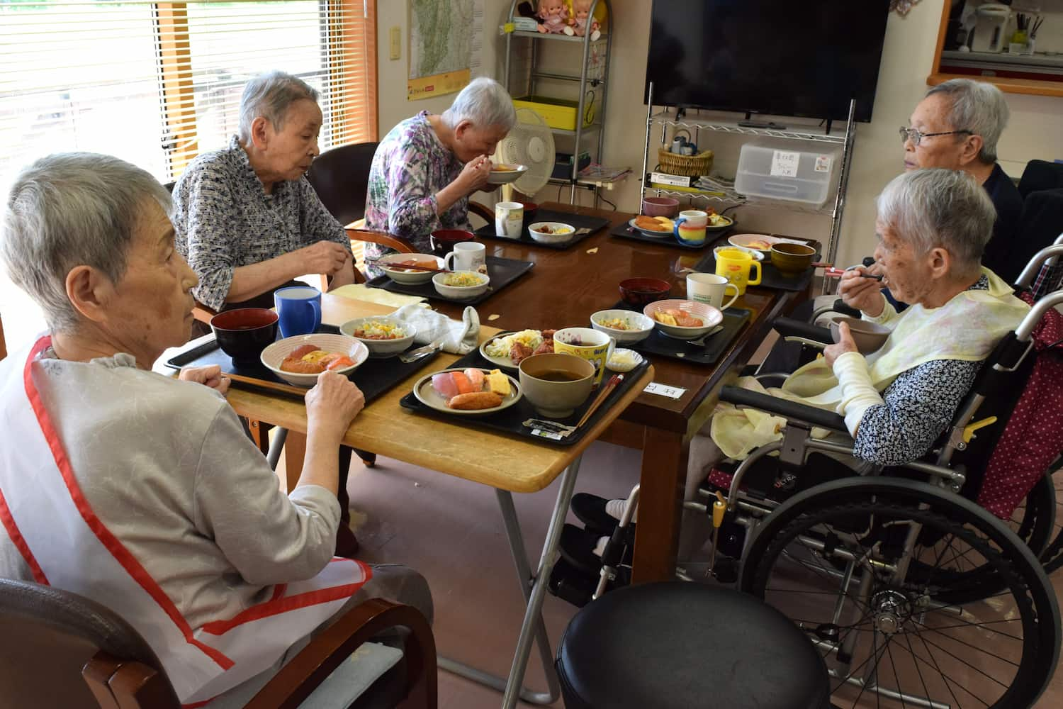 窓際のテーブルでは入居者さん5人が囲んで食べています。