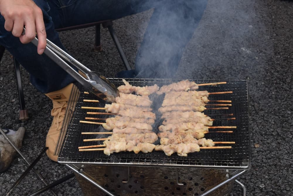 網の上で、20本以上の焼き鳥を、トングを使って焼いている所長。焼き鳥には焼き色が付いています。