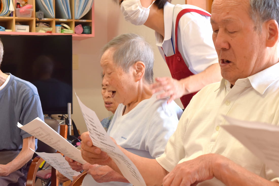 座ったままスタッフに支えられて歌う入居者さん。