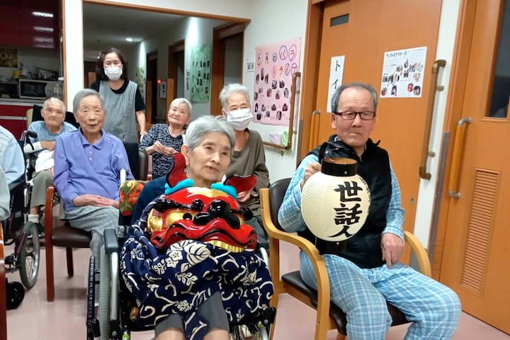 獅子舞の被り物と「世話人」と書かれた提灯を持てせてもらい、うれしそうな入居者さん