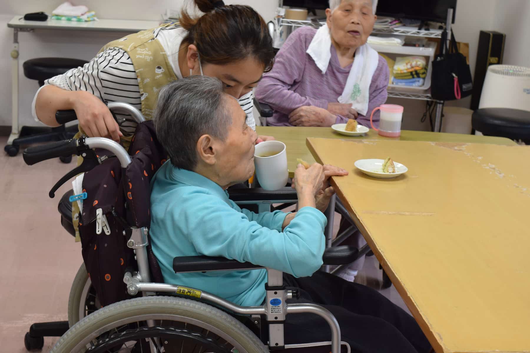 スタッフに介助されながら、お茶を飲む入居者さん。