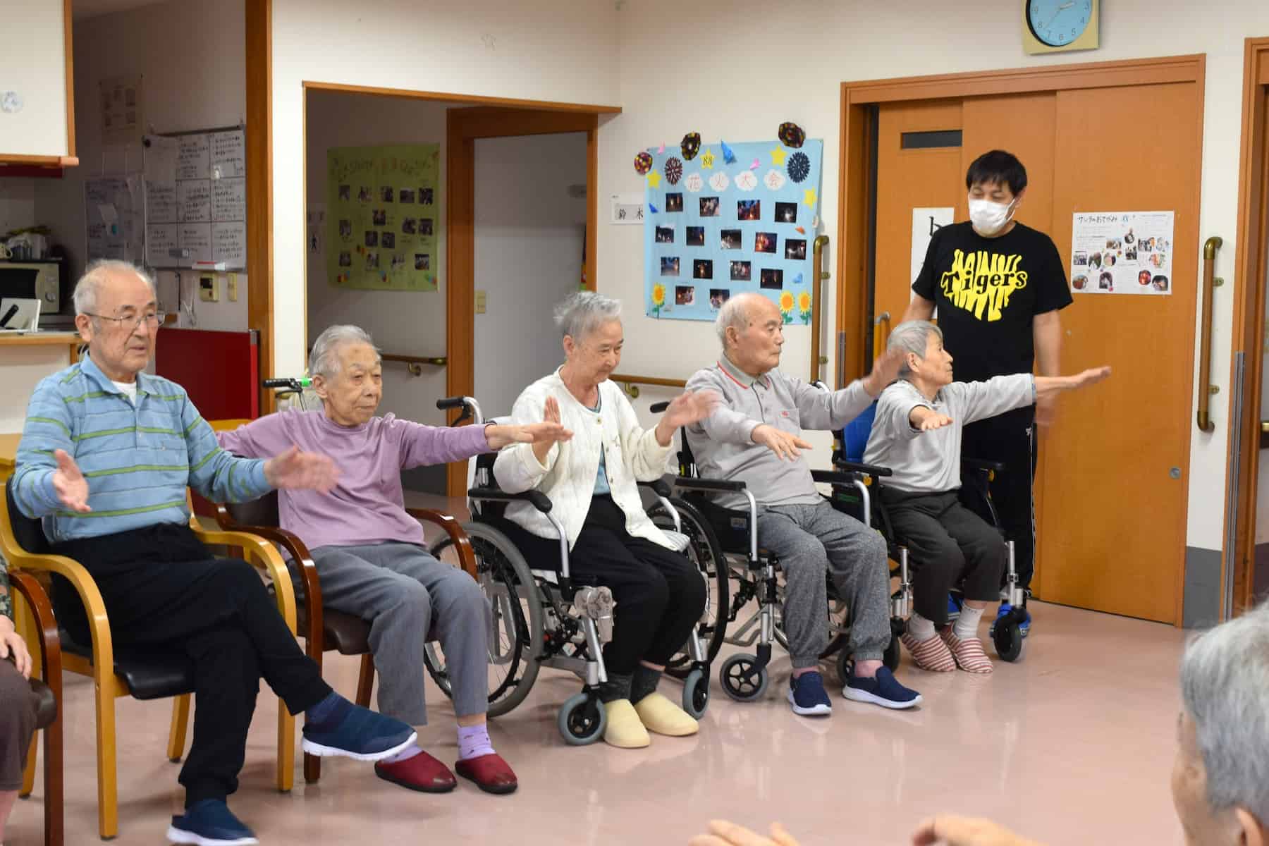 入居者さんが一列に向き合って座り、手を伸ばしてウォーミングアップしています。