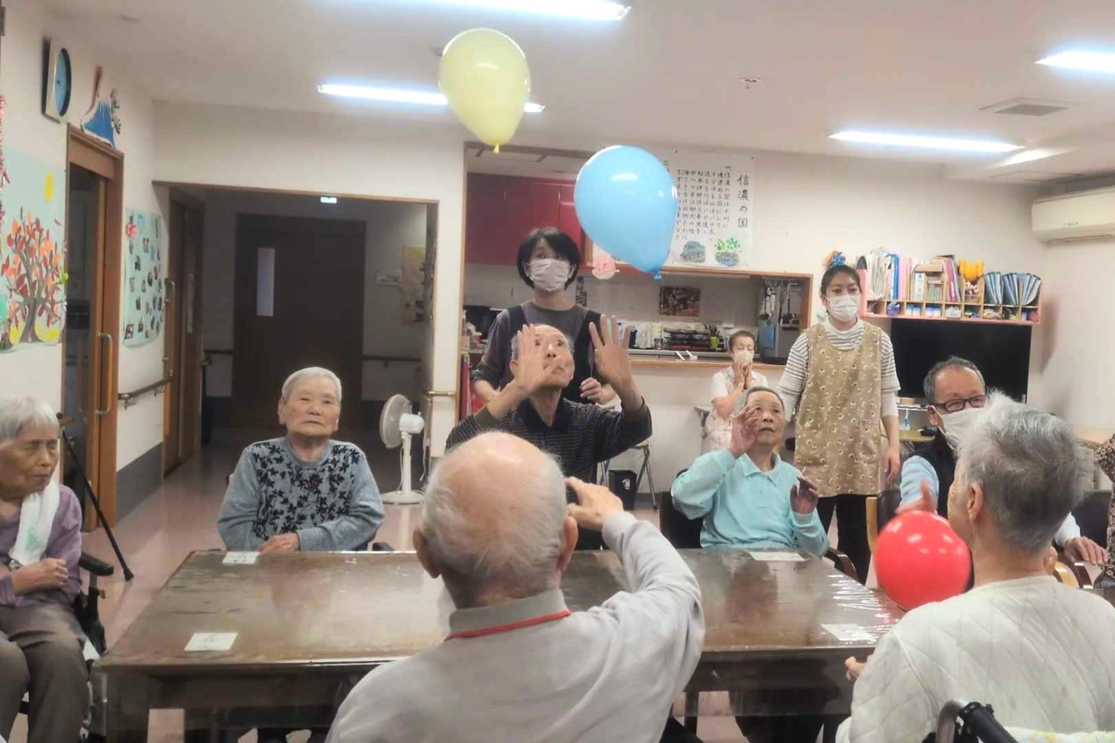 椅子に座った入居者さんたちが手を伸ばし、風船を打とうとしています。
